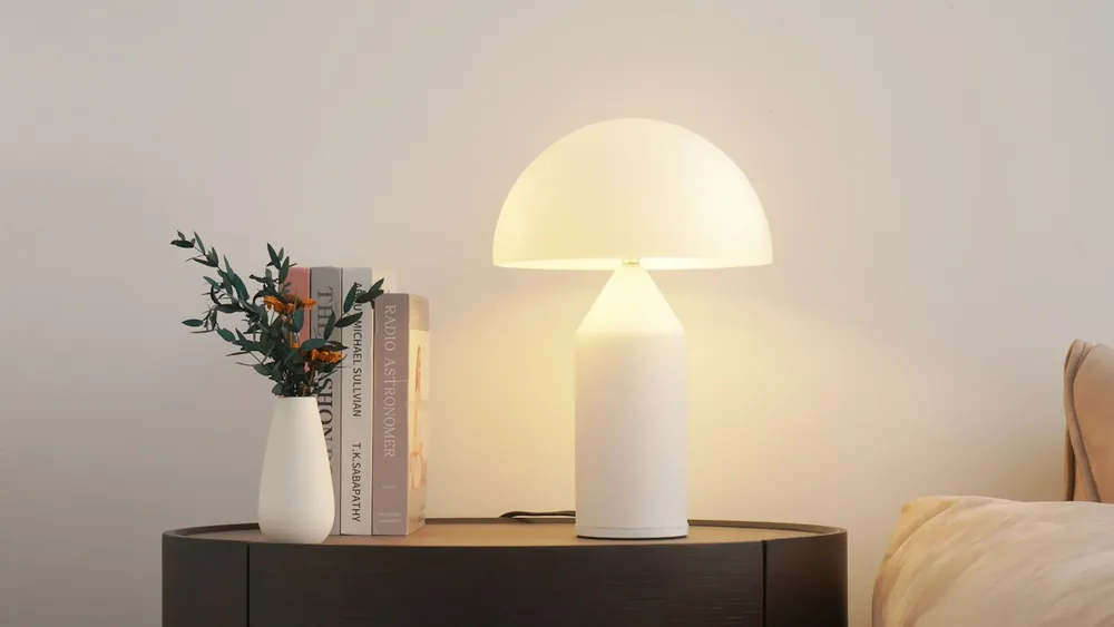 A glowing table lamp beside a vase and books